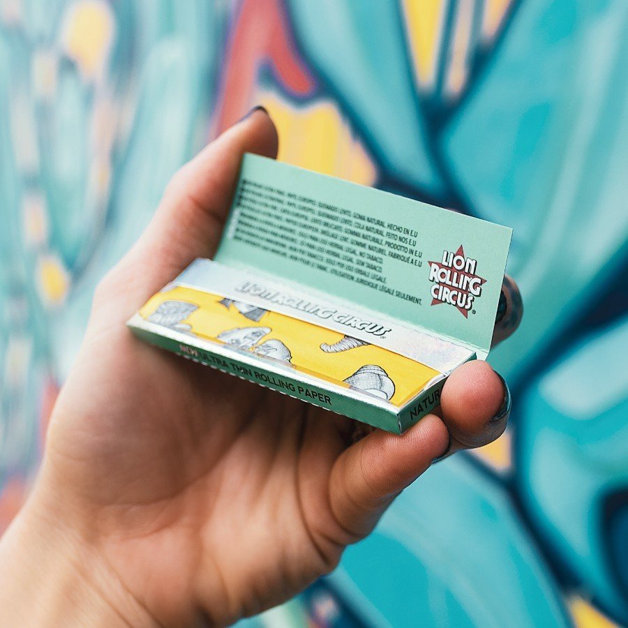 Cueros Papeles Lion Rolling Circus Ultra Thin #9 Silver en la mano frente a un mural de grafiti