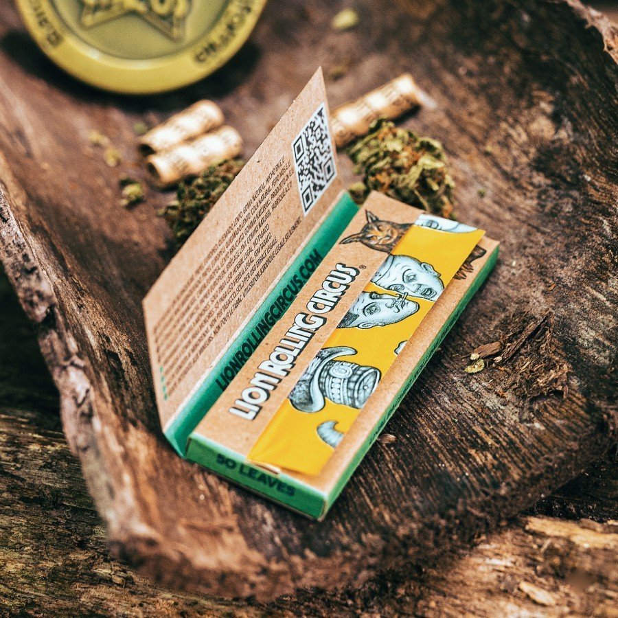 Cueros Papeles Lion Rolling Circus Unbleached #9 abiertos sobre un tronco junto a filtros enrollados y un grinder